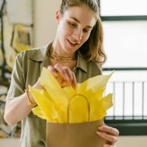 Adult woman showcasing her craft business skills by packing a gift with yellow tissue paper.