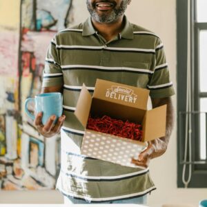 Entrepreneur holding a delivery box and mug, showcasing a small business environment.